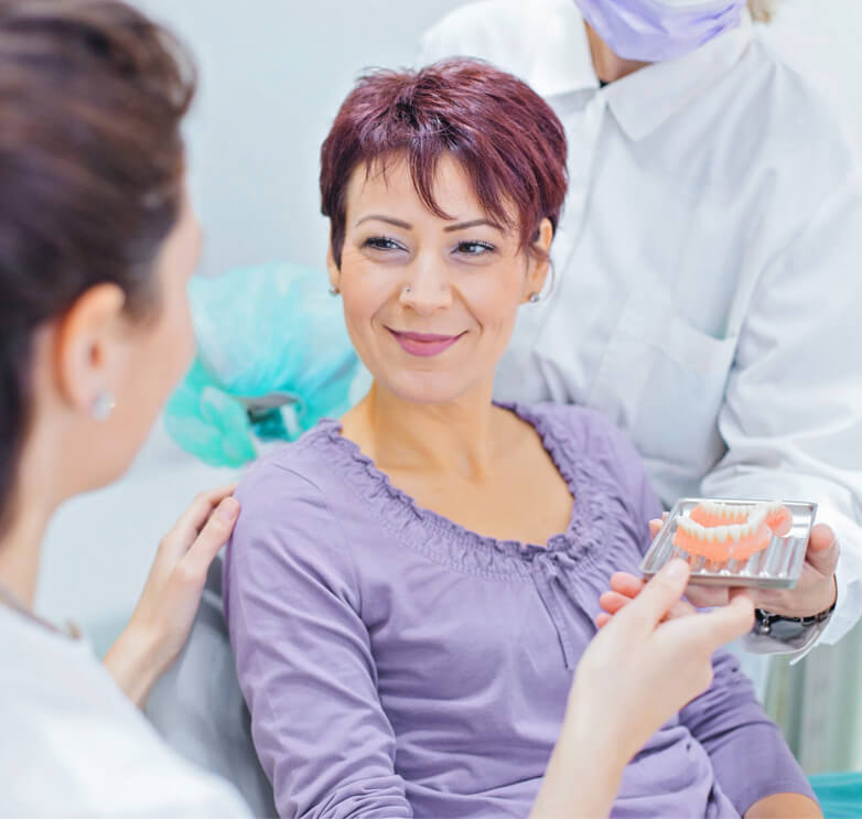 Female dentist talking to a patient and showing her teeth dentures